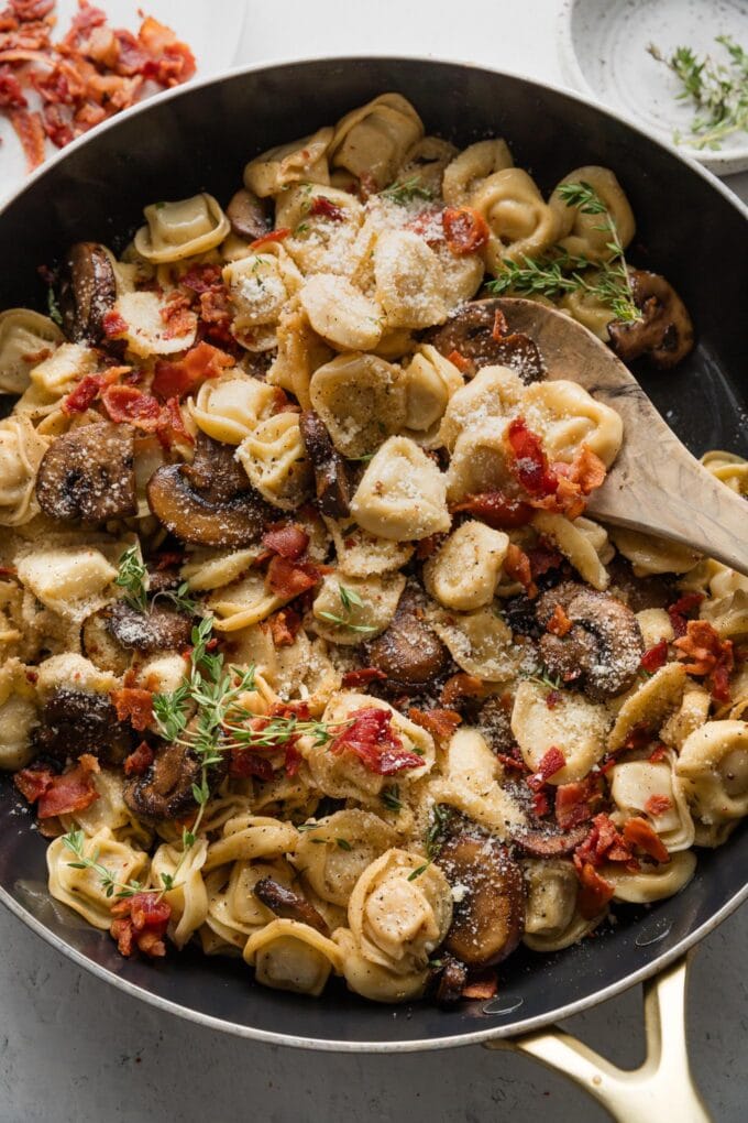 Spoon lifting up a portion of tortellini with mushrooms and bacon.