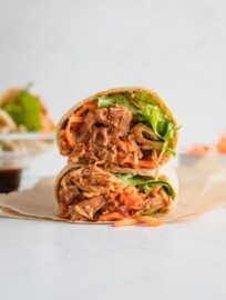 BBQ chicken wrap cut open to reveal the tender shredded chicken, crisp green leaf lettuce, and carrots inside.