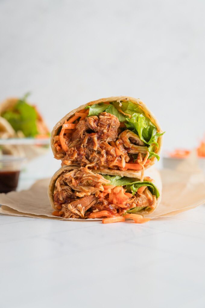 BBQ chicken wrap cut open to reveal the tender shredded chicken, crisp green leaf lettuce, and carrots inside.