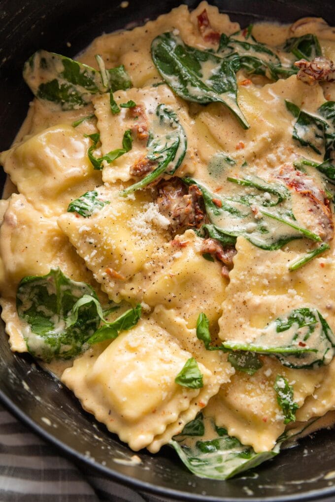 Creamy Tuscan ravioli finished in a deep cast iron skillet.
