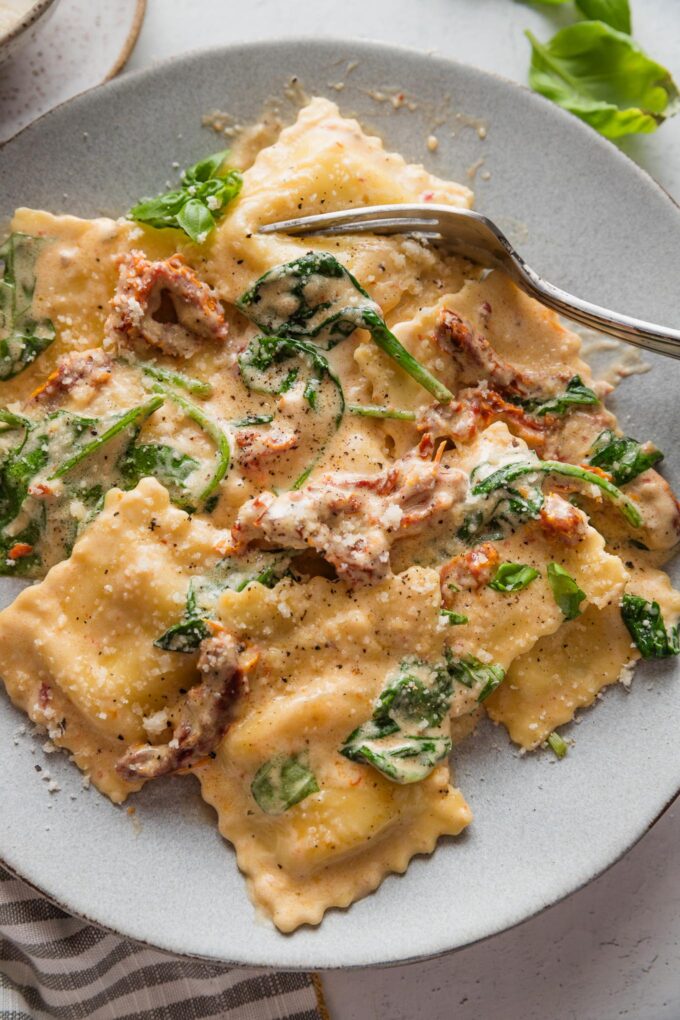 Plate full of creamy Tuscan ravioli with a garlicky sun-dried tomato cream sauce and baby spinach and Parmesan.
