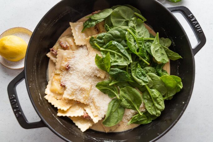 Baby spinach and grated Parmesan added to ravioli cooked in a skillet.