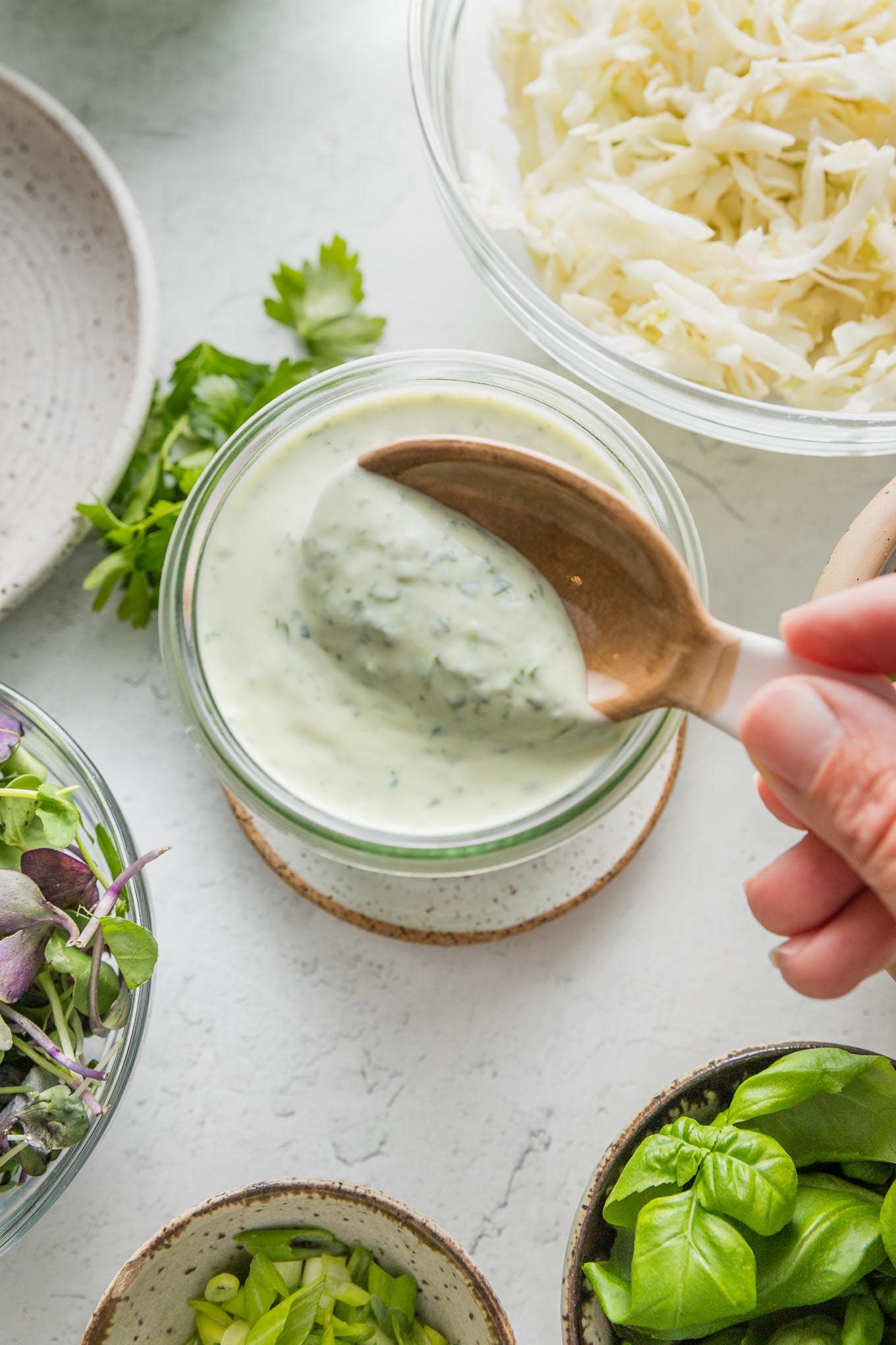 Close-up of homemade green goddess dressing in a small glass jar being lifted out with a small ceramic spoon.