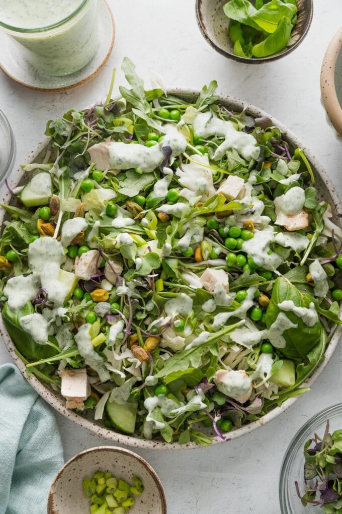 Countertop set with a large green goddess salad surrounded by extra homemade dressing, microgreens, herbs, and pistachios.