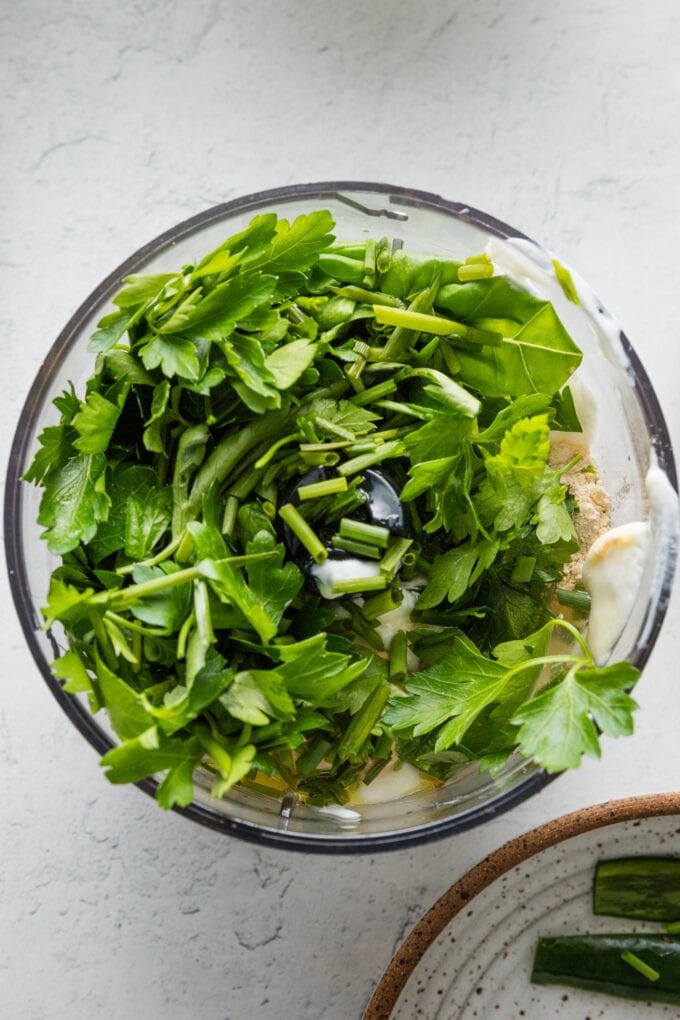 Herbs and yogurt added to the bowl of a small food processor.