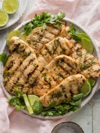 Large plate of grilled chicken marinated in cilantro lime juice seasoned with cumin, honey, and salt, garnished with lime wedges and fresh cilantro.