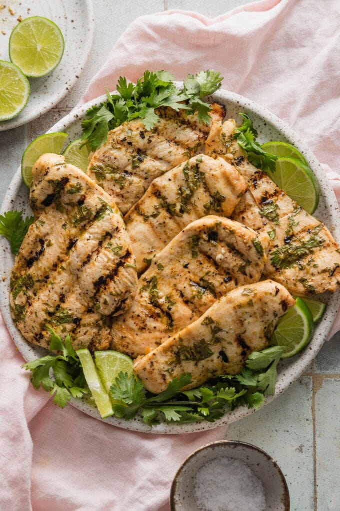 Large plate of grilled chicken marinated in cilantro lime juice seasoned with cumin, honey, and salt, garnished with lime wedges and fresh cilantro.