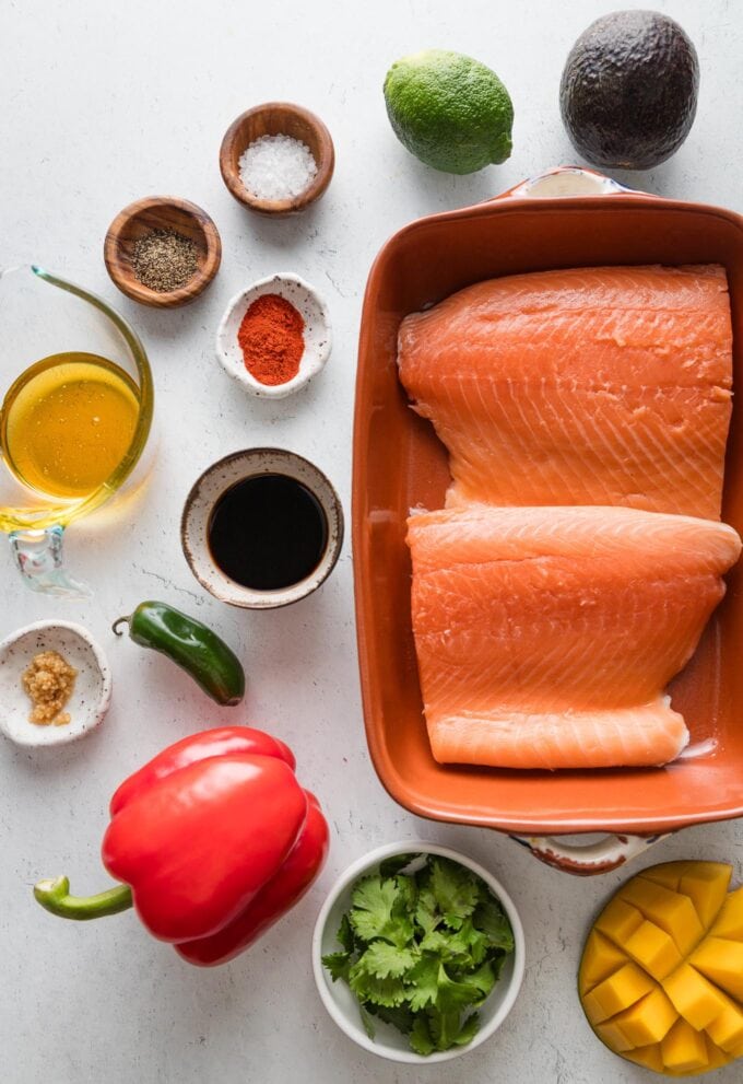 Overhead view of two large salmon filets in a small baking dish plus the ingredients for a honey lime soy sauce and mango salsa.