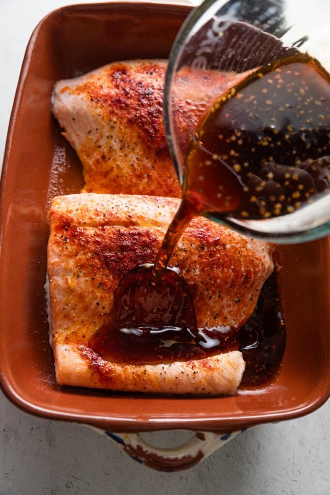 Honey lime soy sauce mixture being poured from a liquid measuring cup over seasoned salmon filets.