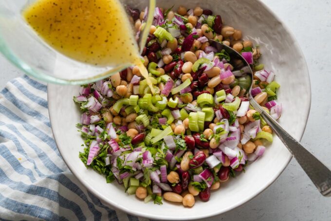 Action shot of a homemade dressing being poured out of a glass liquid measuring cup and over a bean salad.