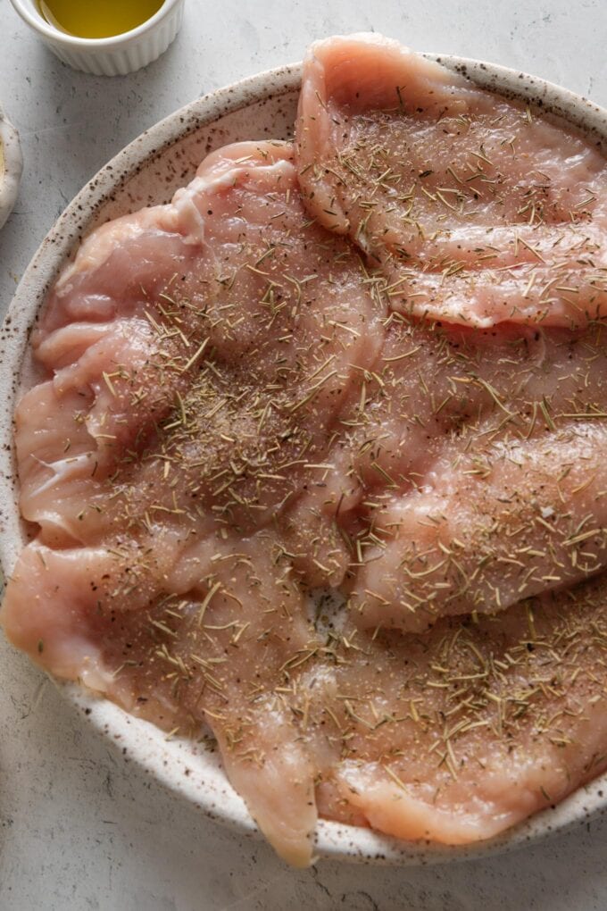 Seasoned, uncooked chicken breasts resting on a plate.