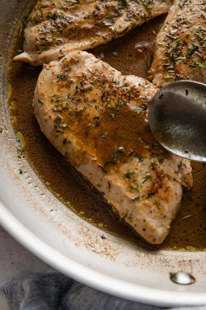 Close up of a spoon drizzling sauce over a chicken breast.