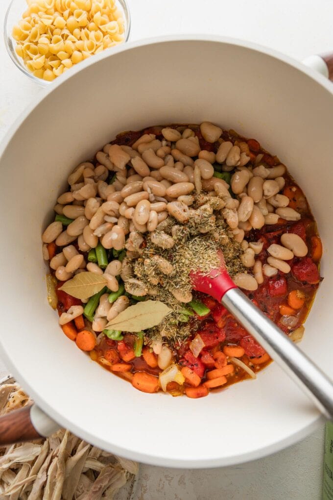 Base of a minestrone soup with sauteed carrots and onion, bay leaves and other seasonings, and white beans in a stock pot.
