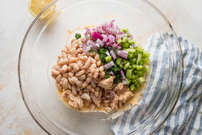 Tuna salad ingredients added to dressing in a large glass prep bowl.
