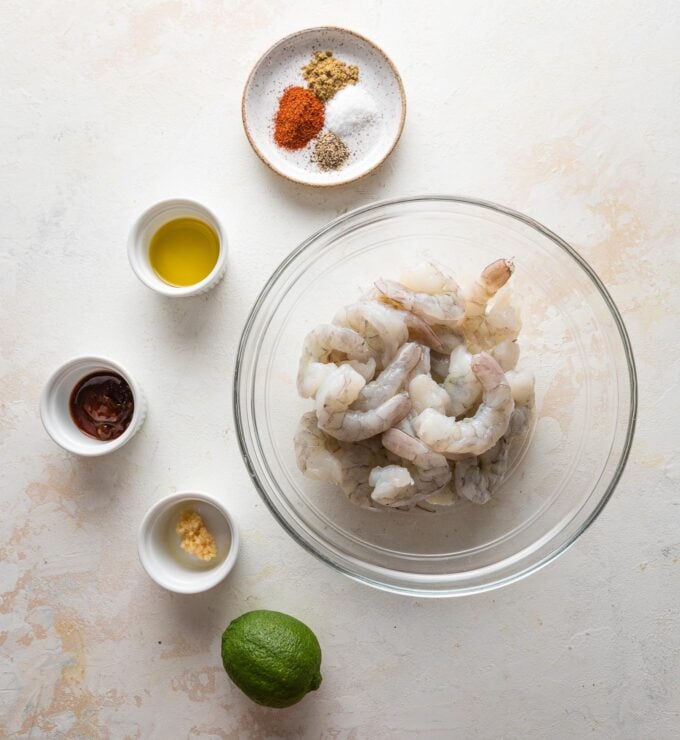 Prep bowls full of raw shrimp, olive oil, lime, adobo sauce, garlic, and dried spices.