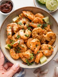 Woman's hand holding up a bowl full of chipotle seasoned baked shrimp.