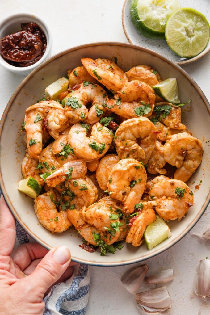Woman's hand holding up a bowl full of chipotle seasoned baked shrimp.