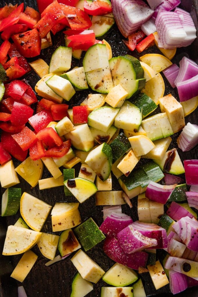 Chopped summer veggies drizzled with olive oil and balsamic on a baking tray.
