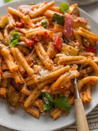 Close up of a plate filled with sun-dried tomato pesto pasta with shredded rotisserie chicken and roasted veggies mixed in.