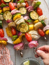 A woman's hand picking up a veggie skewer off of a plate.