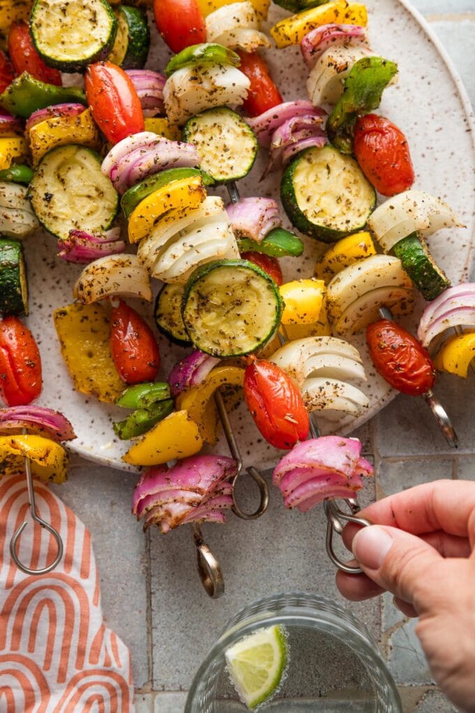 A woman's hand picking up a veggie skewer off of a plate.