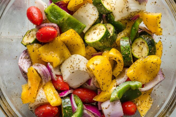 Veggies for skewers chopped into a mostly even size and seasoned in a prep bowl with olive oil, Italian seasoning, salt, and pepper.