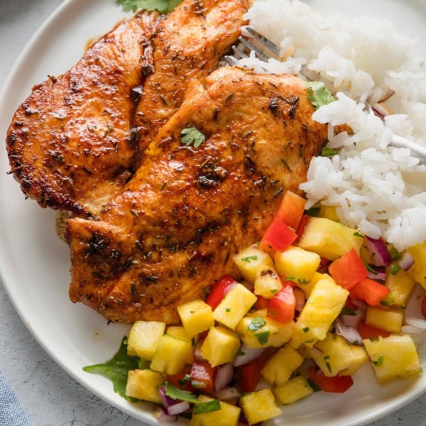 Plate of chicken cutlets pan-seared with a brown sugar spice rub, pineapple salsa, and rice.