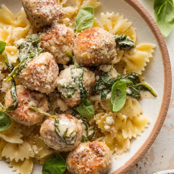 Small bowl full of bowtie pasta topped with chicken Florentine meatballs with a cream sauce.