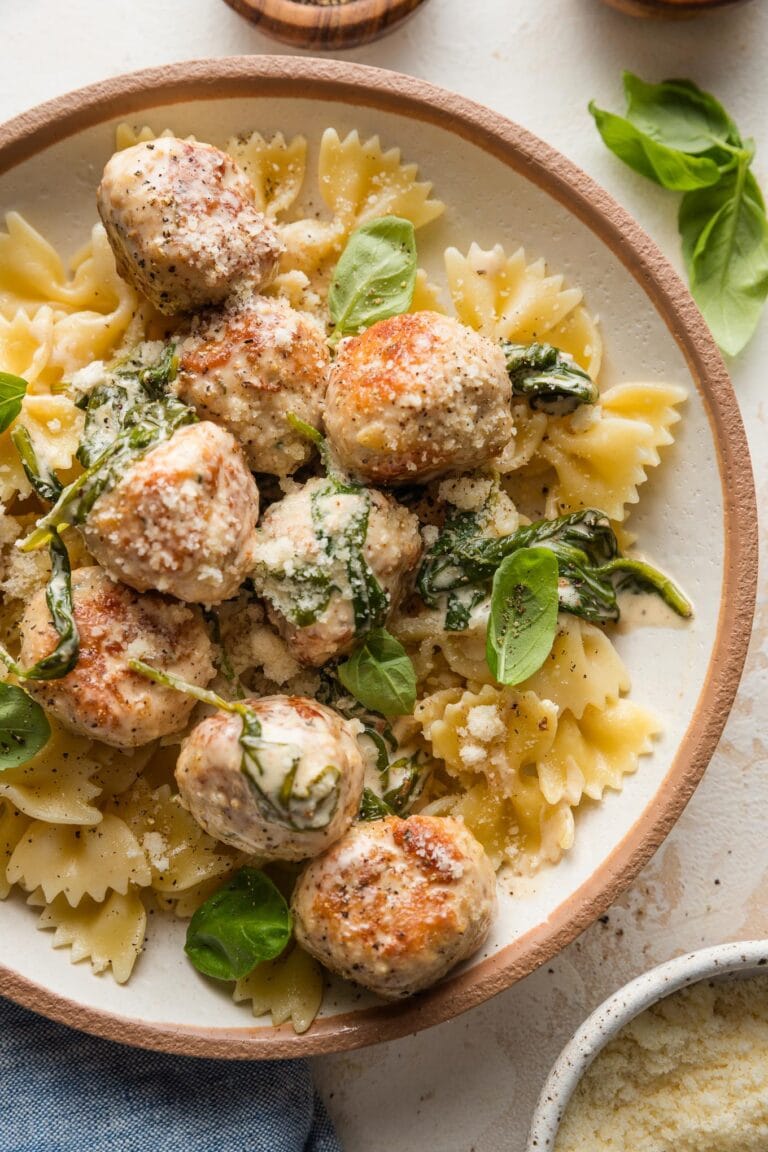 Small bowl full of bowtie pasta topped with chicken Florentine meatballs with a cream sauce.