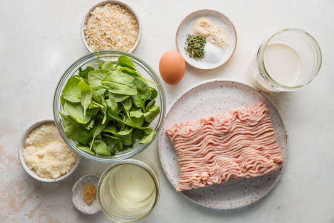 Overhead image of ground chicken, baby spinach, garlic, cream, broth, white wine, and spices for chicken Florentine meatballs.