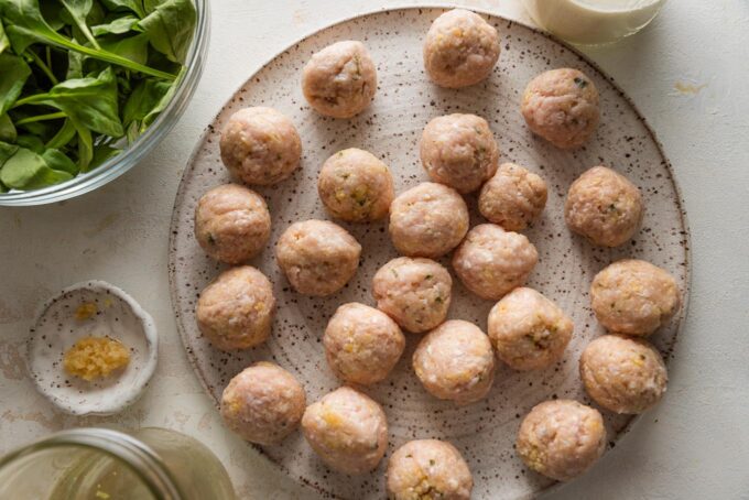 Chicken meatballs rolled into balls but not yet cooked, resting on a dinner plate.