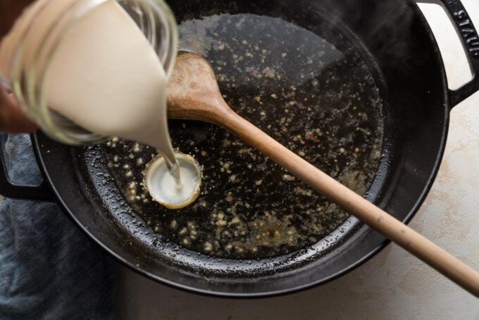 Cream being poured into a white wine sauce in a skillet.
