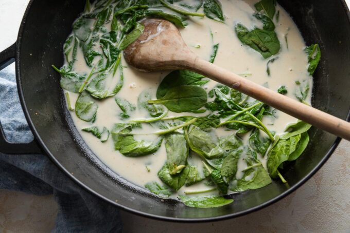 Spinach being stirred into a light cream sauce.