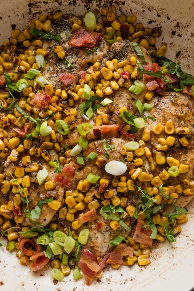 Skillet full of chicken with brown butter corn, bacon, and fresh basil and thyme.