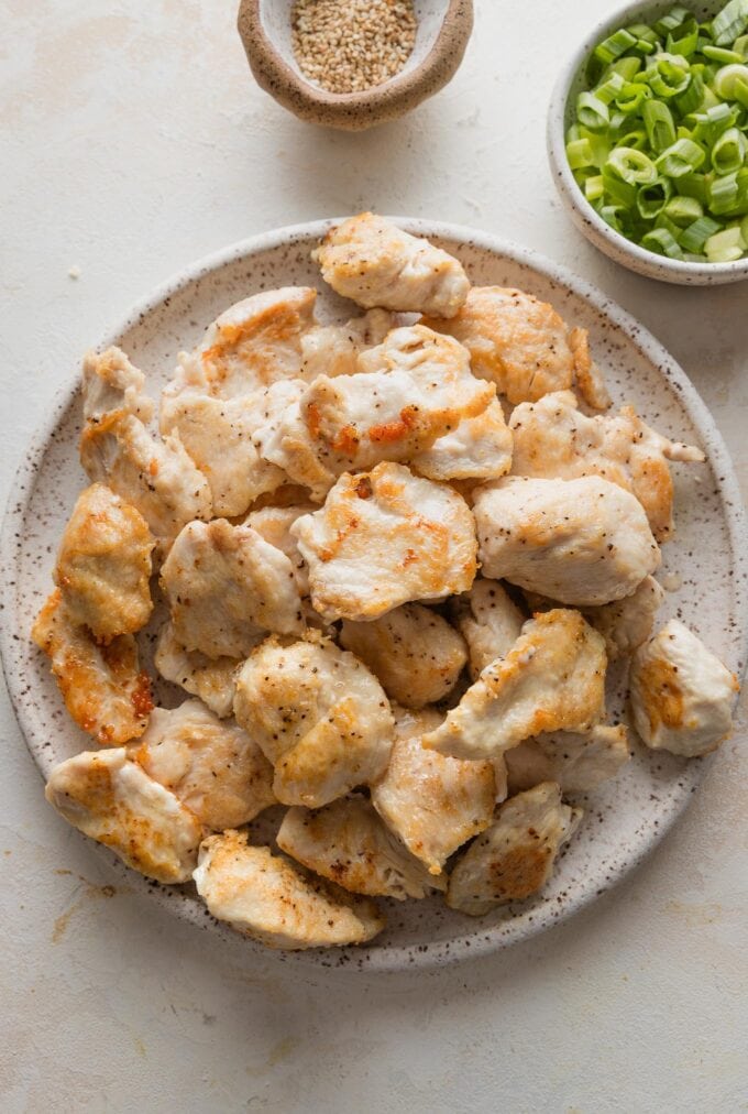 Pieces of cornstarch-coated chicken breast pan-fried to a golden exterior and removed to rest on a plate.