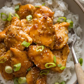 Close up of a bowl of homemade Asian-inspired orange chicken topped with green onions and sesame seeds.