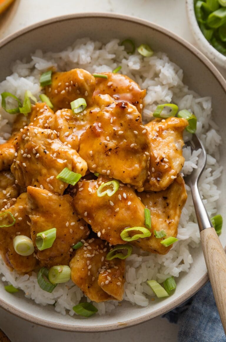 Close up of a bowl of homemade Asian-inspired orange chicken topped with green onions and sesame seeds.