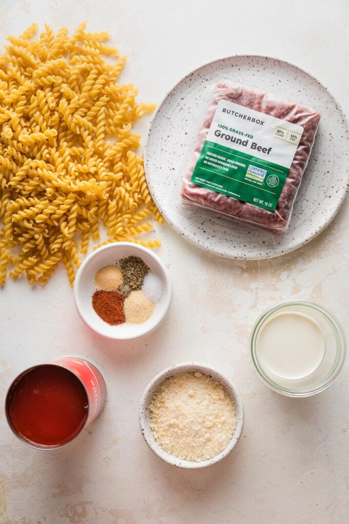 Overhead view of the ingredients for an extra easy rotini pasta recipe: ground beef, tomato sauce, dried spices, and rotini, of course.