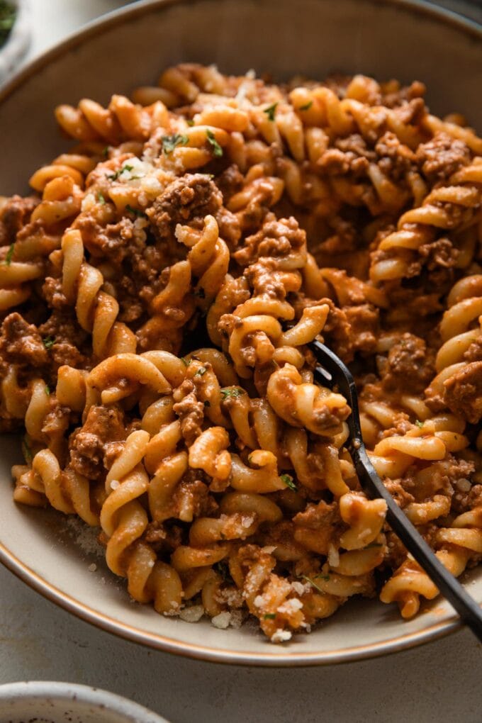 Close up of a fork picking up a bite of rotini pasta with homemade tomato sauce.