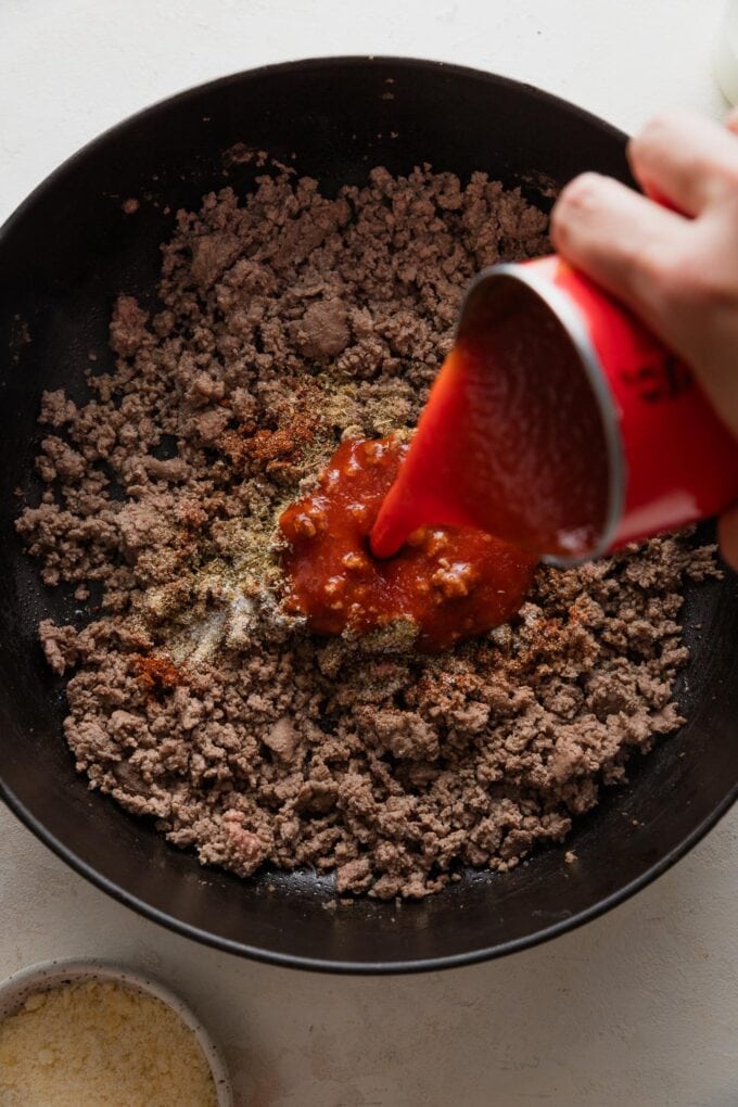 Tomato sauce being poured into browned ground beef.