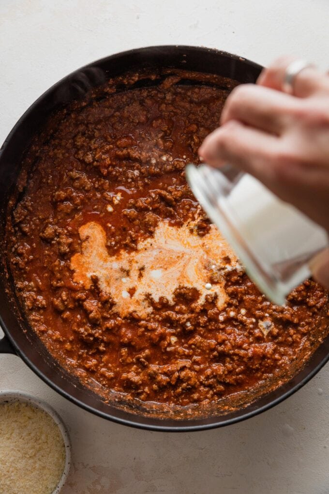 Cream being poured into a homemade tomato meat sauce.
