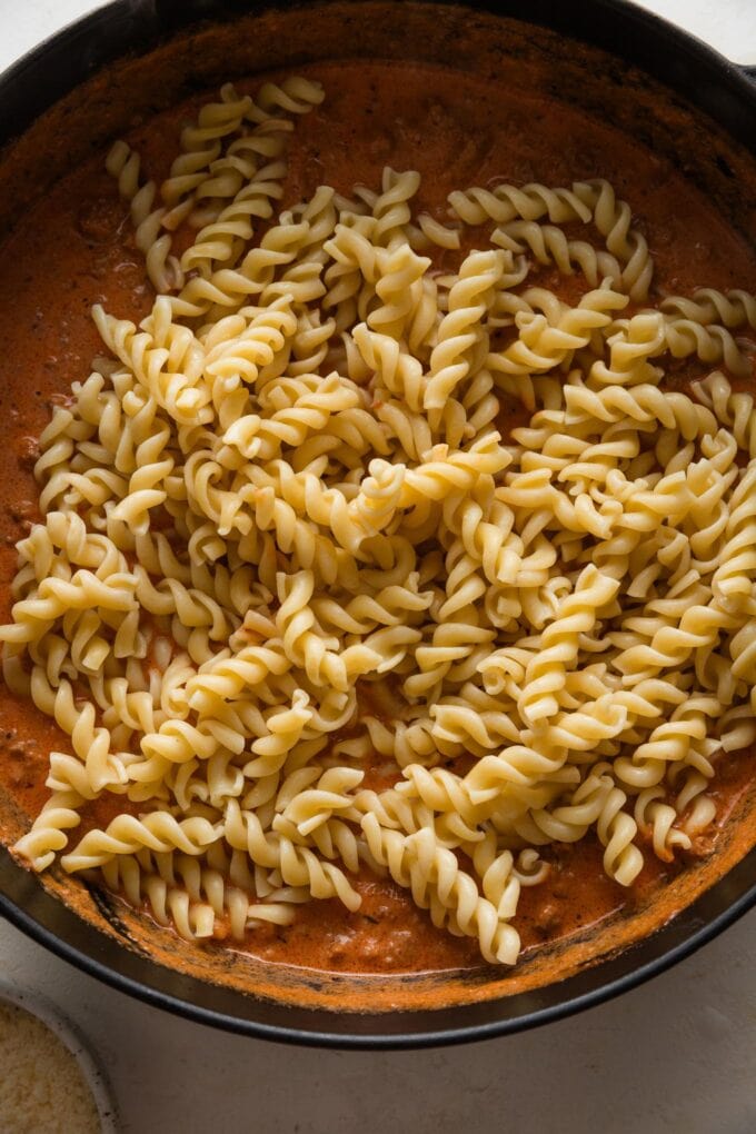 Cooked rotini added to sauce in a skillet.