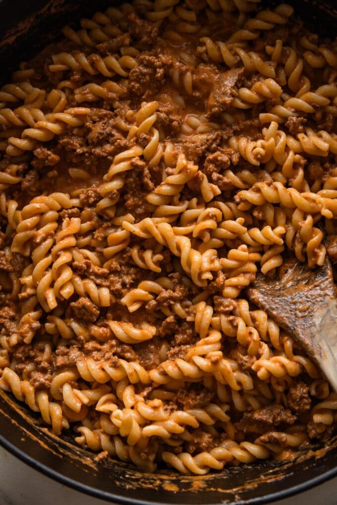 Close up of a wooden spoon stirring rotini into a quick homemade meat sauce.