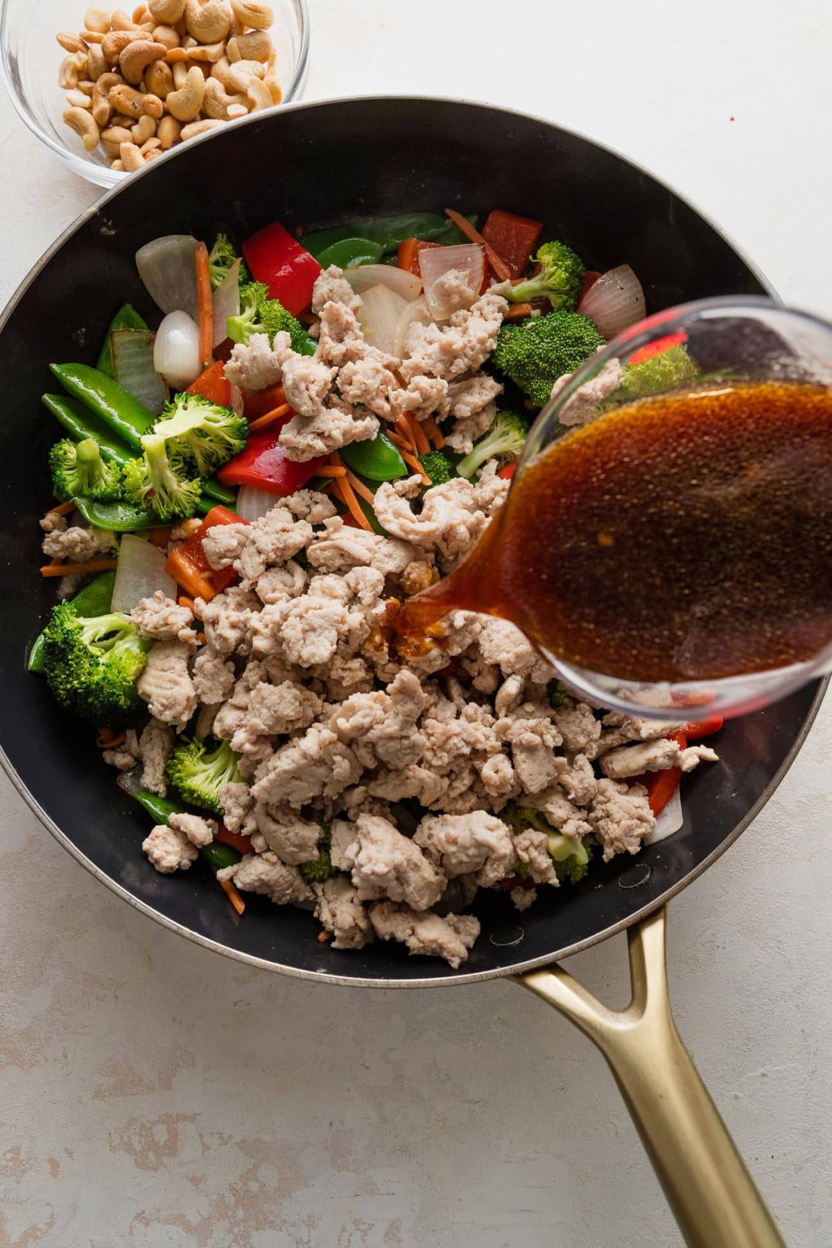 A quick homemade stir fry sauce being poured from a liquid measuring cup into a pan full of cooked ground chicken and veggies.