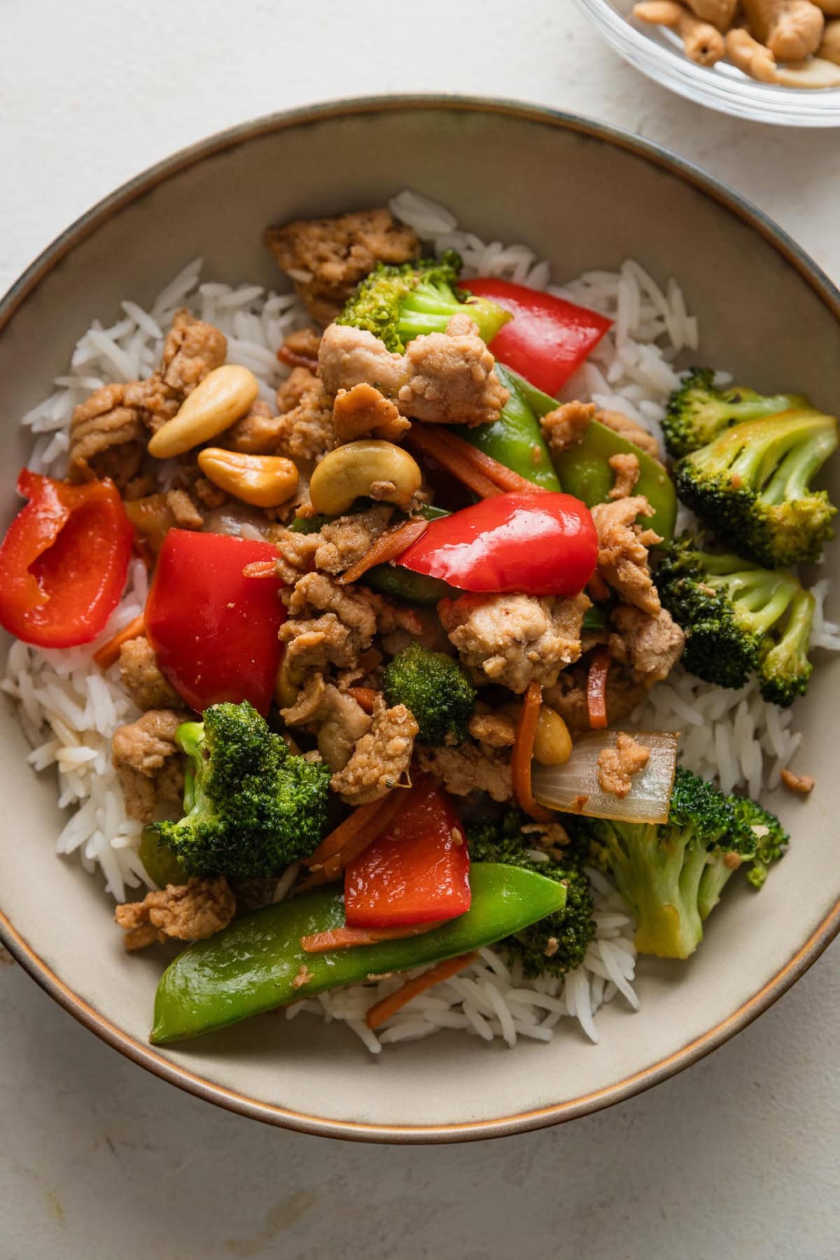 Bowl full of an easy ground chicken stir fry with bell peppers, onions, broccoli, and snow peas served over rice.