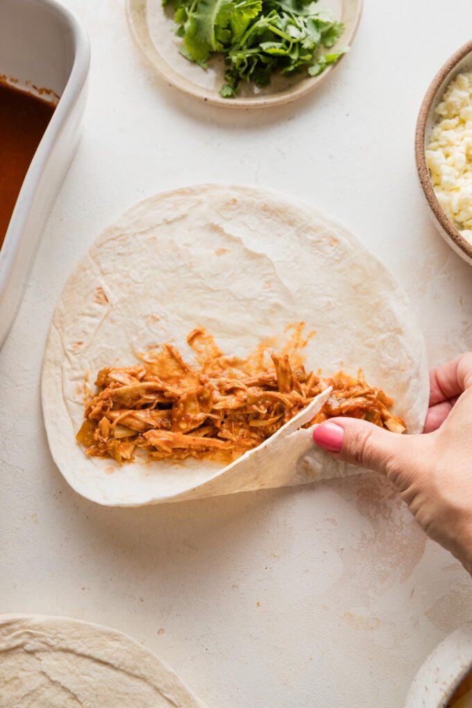 A woman's hand rolling up a chicken enchilada.