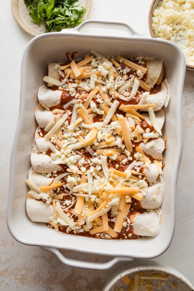 Enchiladas assembled in a baking dish and topped with a final layer of sauce and cheese, ready to bake.