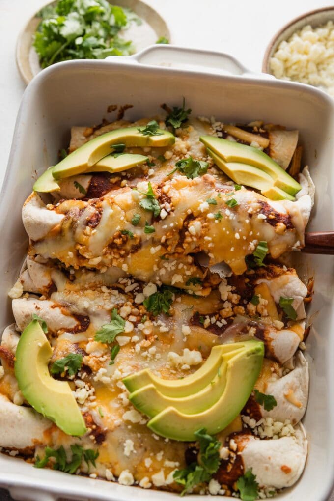 Spatula lifting one chicken enchilada up and out of a pan.