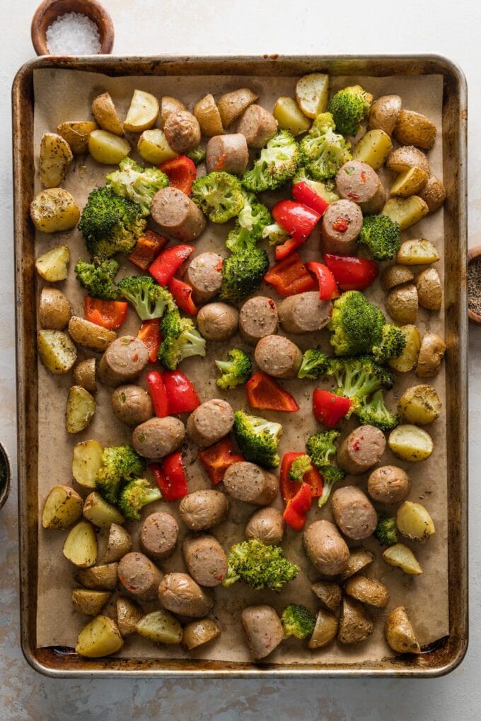 Sheet pan with roasted potatoes around the outside and a sausage, broccoli, bell pepper medley on the inside.