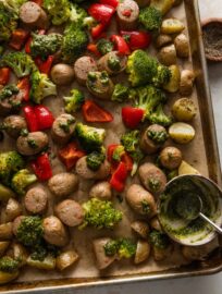Large rimmed sheet pan lined with parchment and filled with a one pan meal of chicken sausage, potatoes, lots of veggies, and pesto.